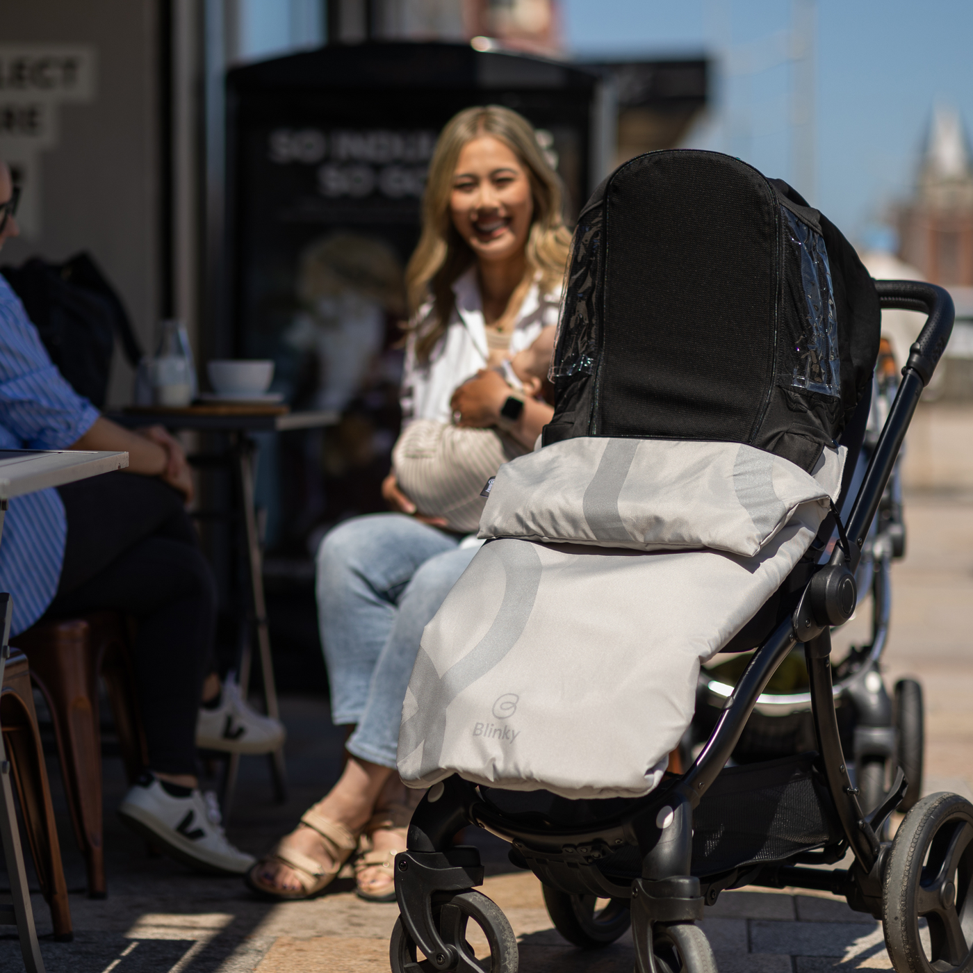 Lady sitting in cafe, close up of stroller with BlinkyWarm in Silver with sun shade up