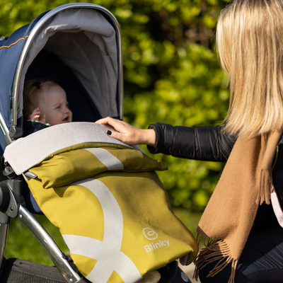 Lady fussing over smiling baby in stroller with BlinkyWarm in Olive