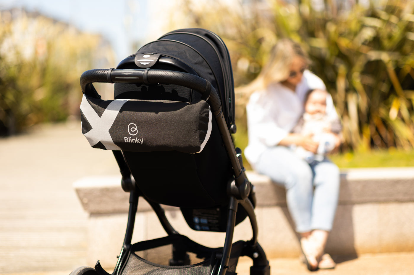 Lady in background with baby, close up of BlinkyWarm in Space packaged up on back of stroller